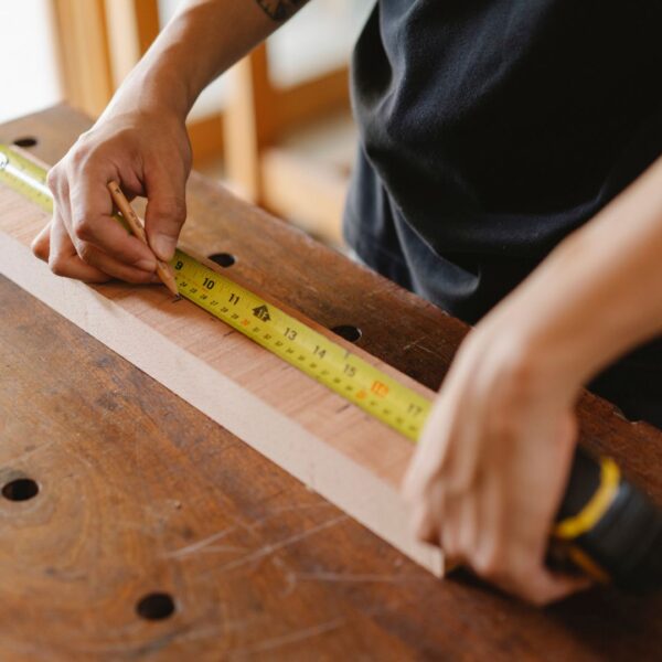 A person's hands holding a tape measure, measuring a wooden board.