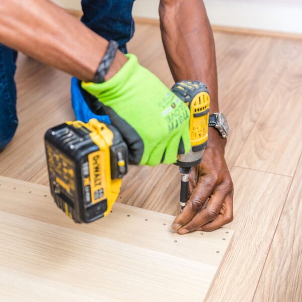 A focused individual is using a power drill to work on a home repair project with sawdust flying.