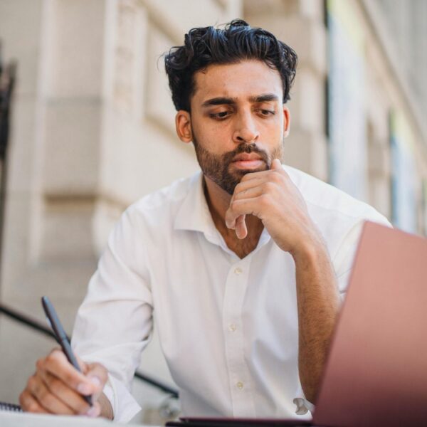 A person is seated at a modern desk, focused on a laptop screen that displays various brand logos, suggesting they are researching different power tool brands.